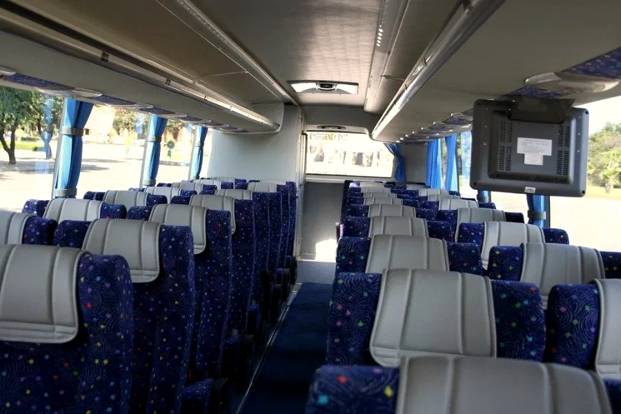 Rows of upholstered seats and an onboard screen inside a Tautona coach