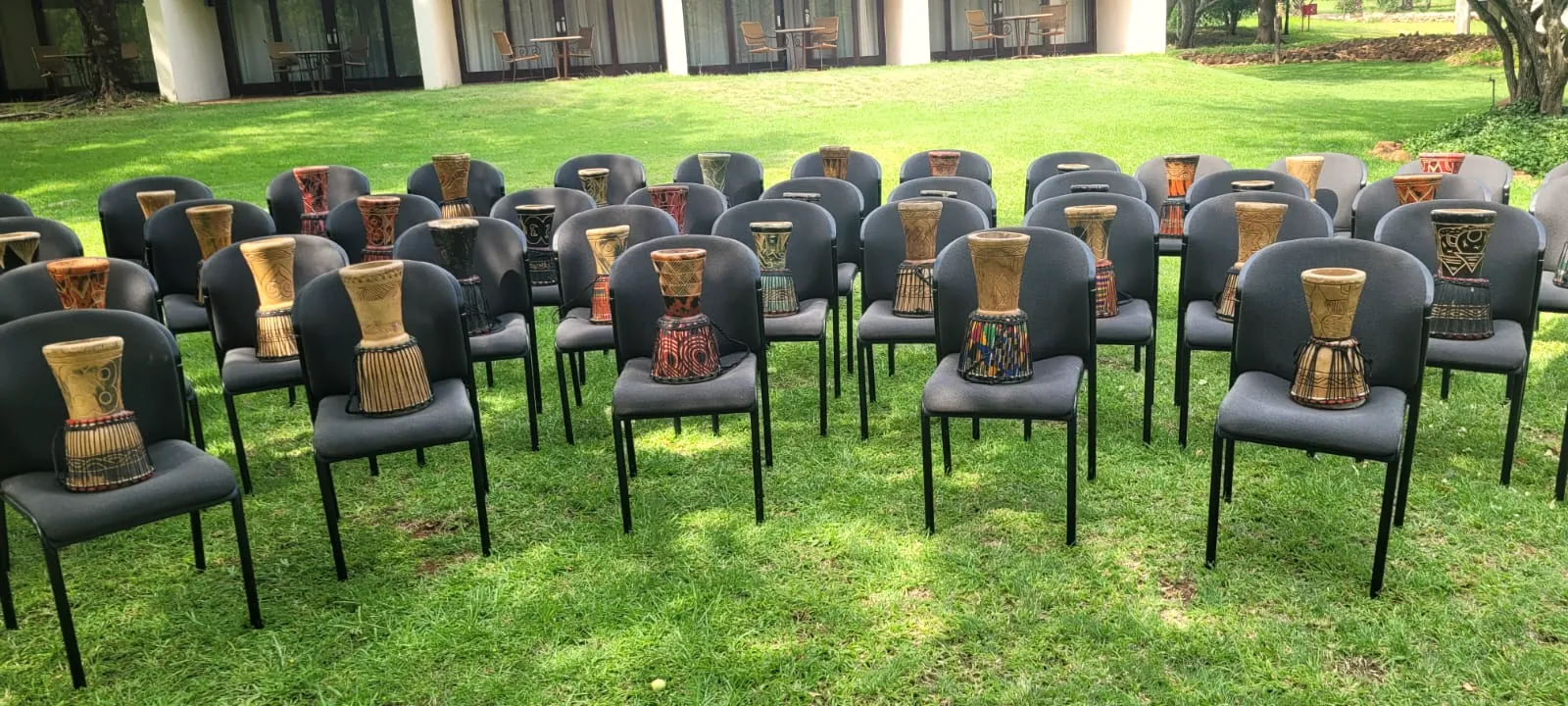 Rows of chairs with djembe drums set out on a lawn for a group session